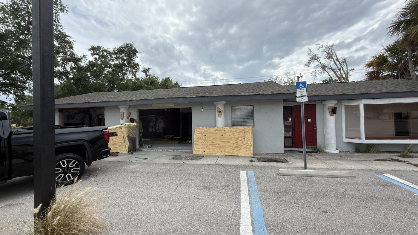 Commercial building before restoration, with boarded windows and damaged exterior